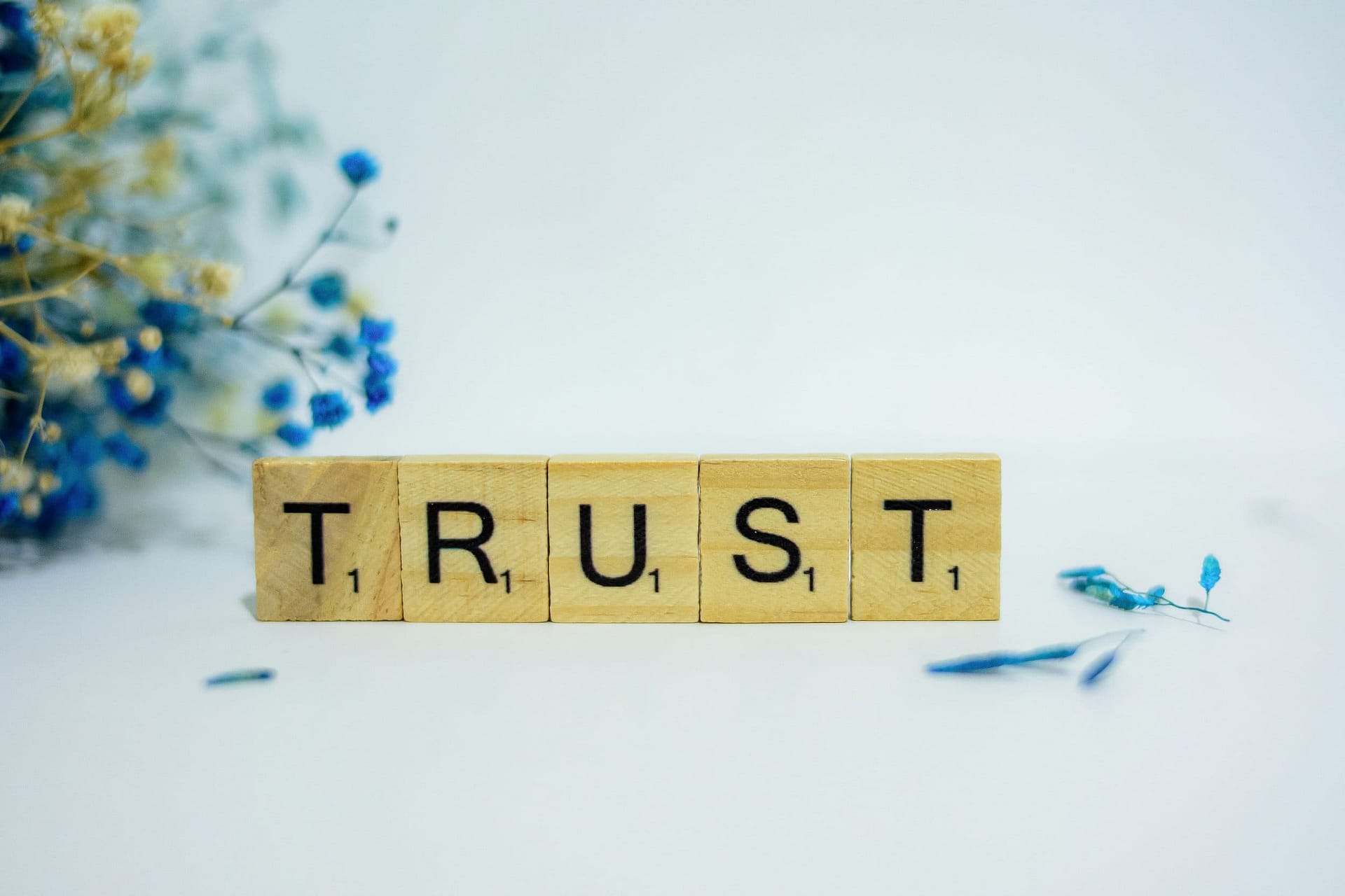 How Does a Trust Work After a Death? 3 Letter tiles spelling the word Trust beside small flowers